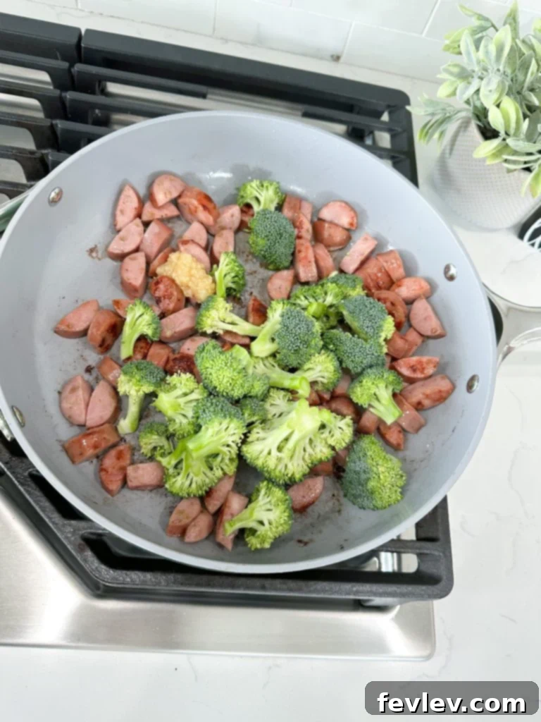 Sautéing minced garlic and fresh broccoli florets with browned chicken sausage in a skillet.