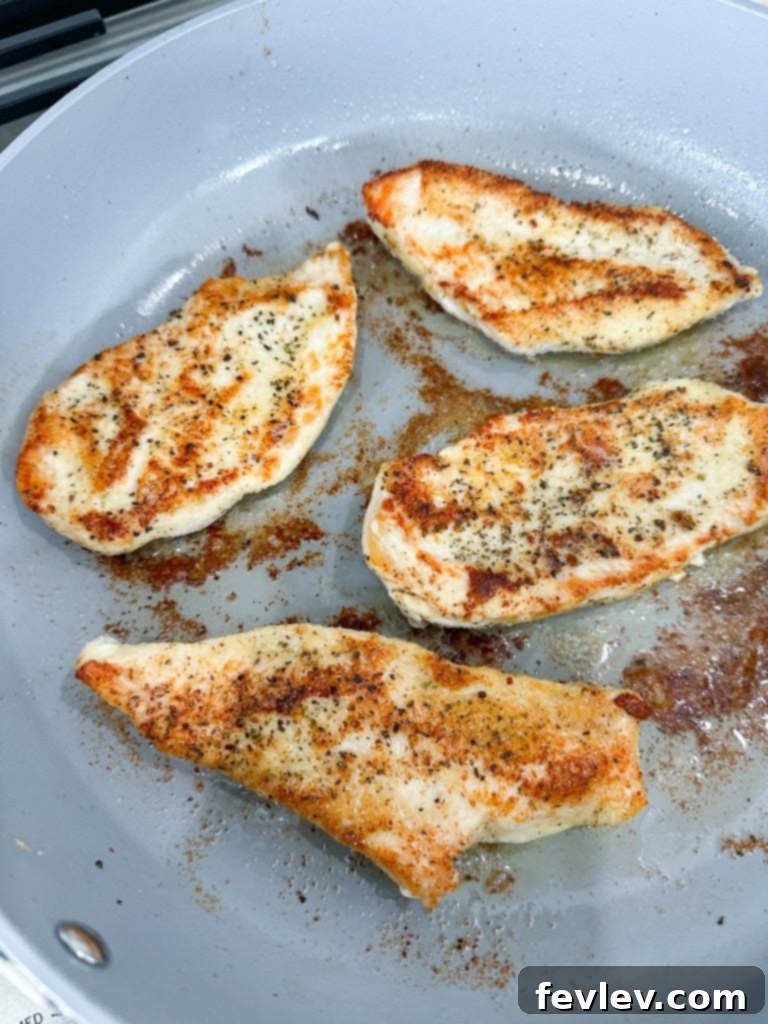 Seasoned chicken breasts browning in a skillet with melted butter and olive oil