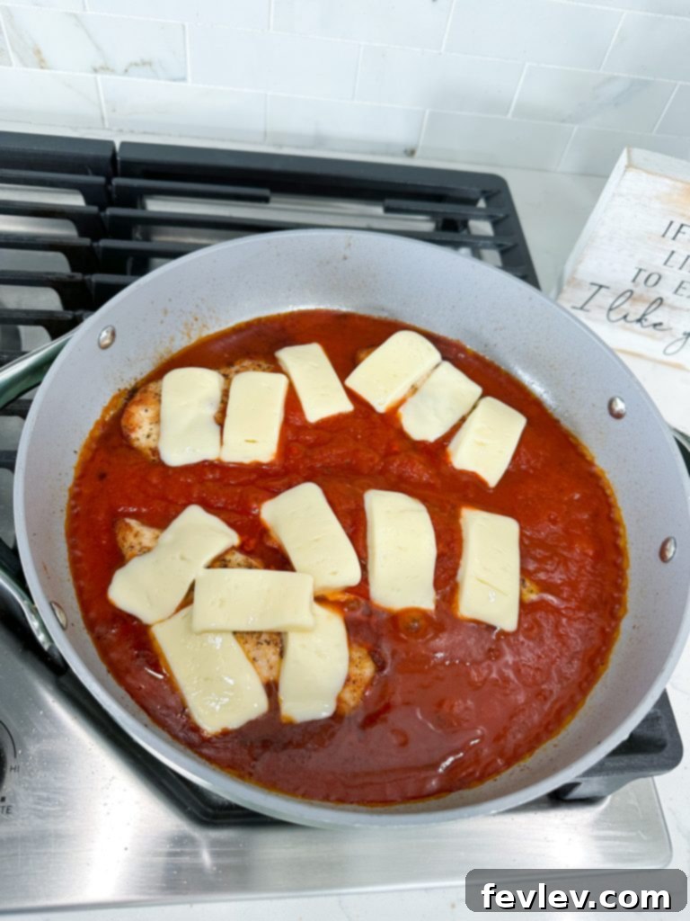 Melted mozzarella cheese generously topping chicken breasts in marinara sauce in a skillet