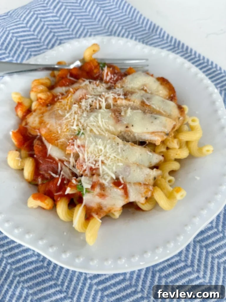 A serving of Chicken Mozzarella Pasta in a bowl, with a chicken breast and melted cheese on top of cellentani pasta