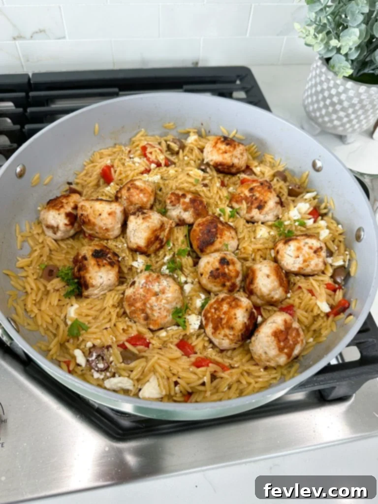 Orzo cooking in a skillet with Mediterranean ingredients