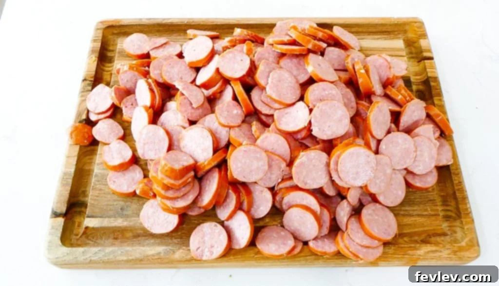 Sliced bell peppers and onions added to potatoes and sausage for sheet pan meal.