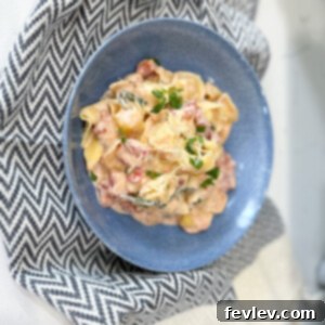 A bowl of creamy tortellini with spinach and diced tomatoes, garnished with fresh herbs.