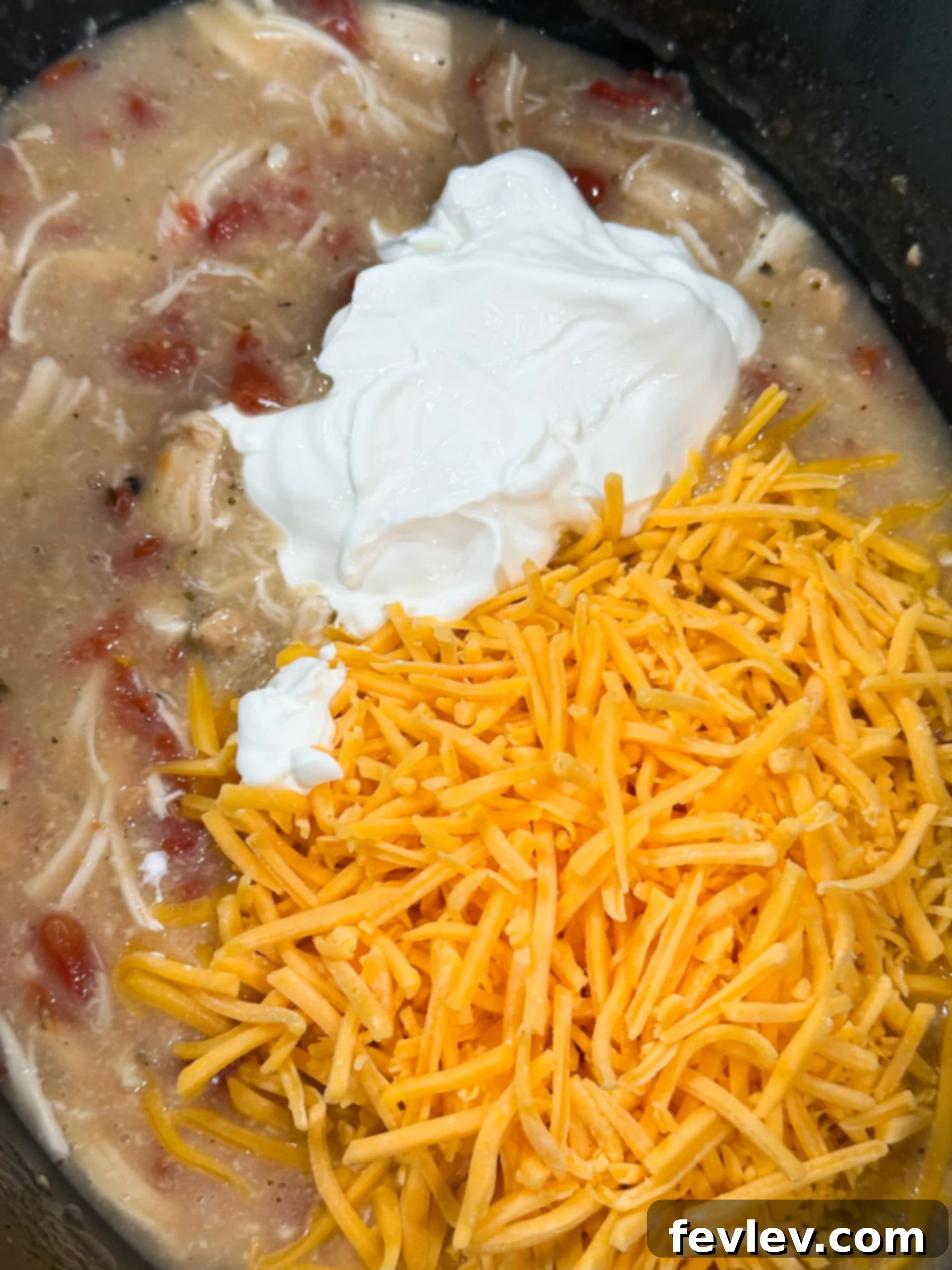 Velvety Slow Cooker Rotel Chicken Pasta 7 Sour cream and shredded cheddar cheese being stirred into the creamy chicken sauce in the slow cooker.