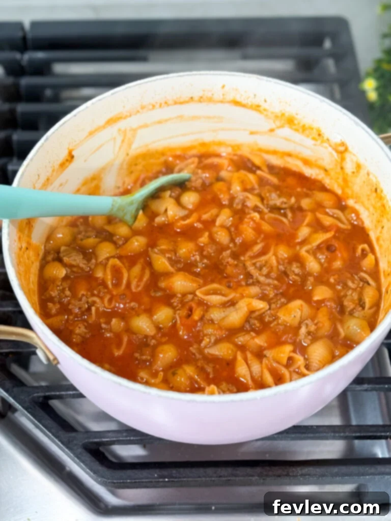 Speedy Skillet Sausage Pasta 4 All ingredients combined in a pot, including marinara sauce, uncooked pasta, and seasonings, ready for simmering.