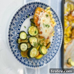 A close-up shot of Sheet Pan Marinara Mozzarella Chicken and Zucchini, featuring a round chicken cutlet topped with marinara and melted mozzarella, served alongside roasted zucchini and yellow squash.