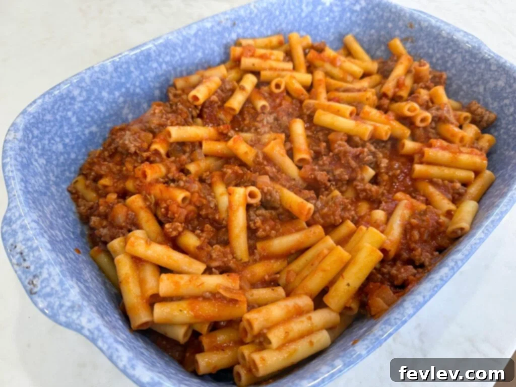 Ultimate Cheesy Baked Ziti 4 Mixing pasta with meat sauce for baked ziti