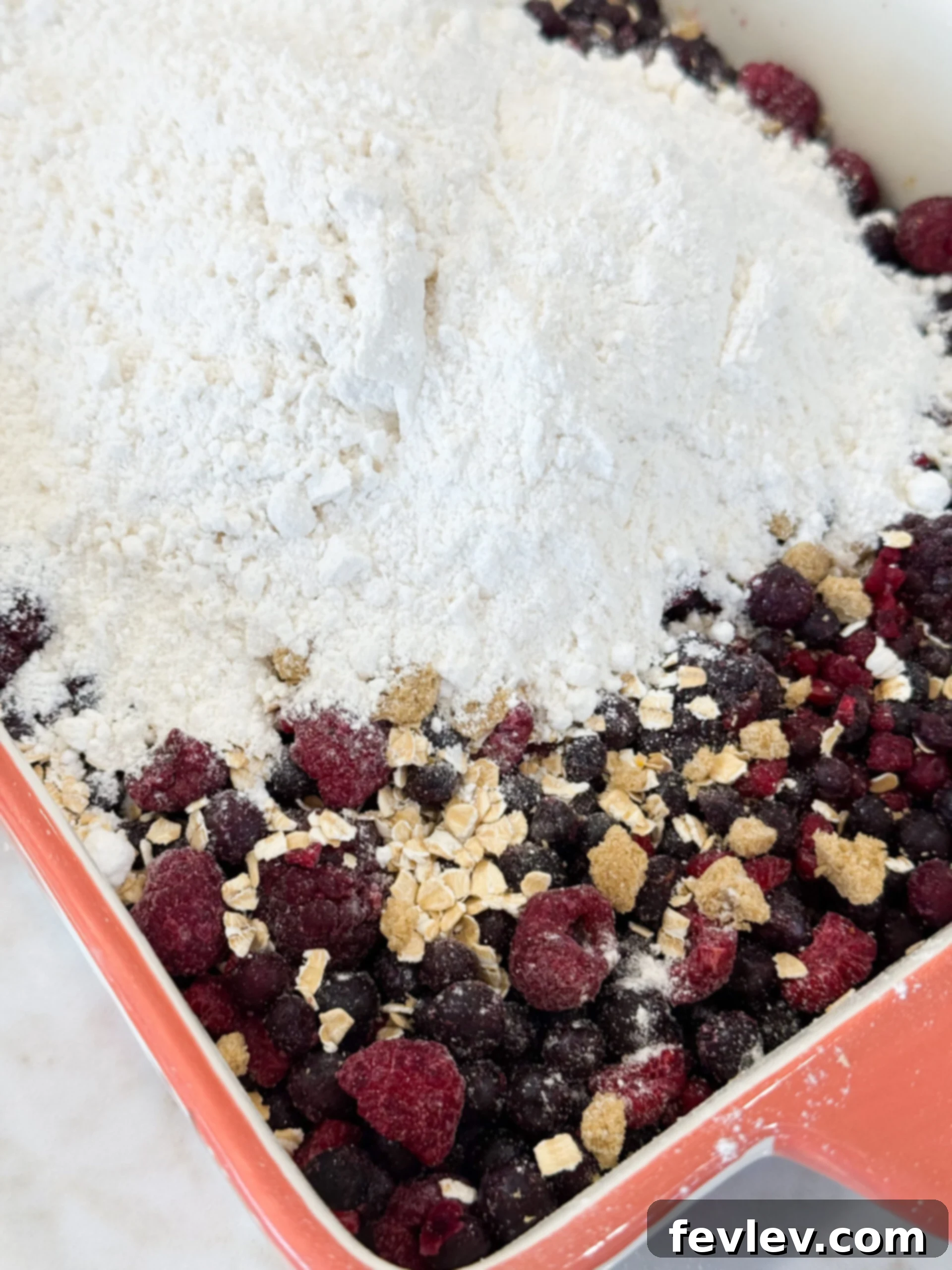 Perfect Homemade Berry Cobbler 6 Layering frozen mixed berries, oats, brown sugar, and dry cake mix in a 9x13 baking dish before baking the berry cobbler.