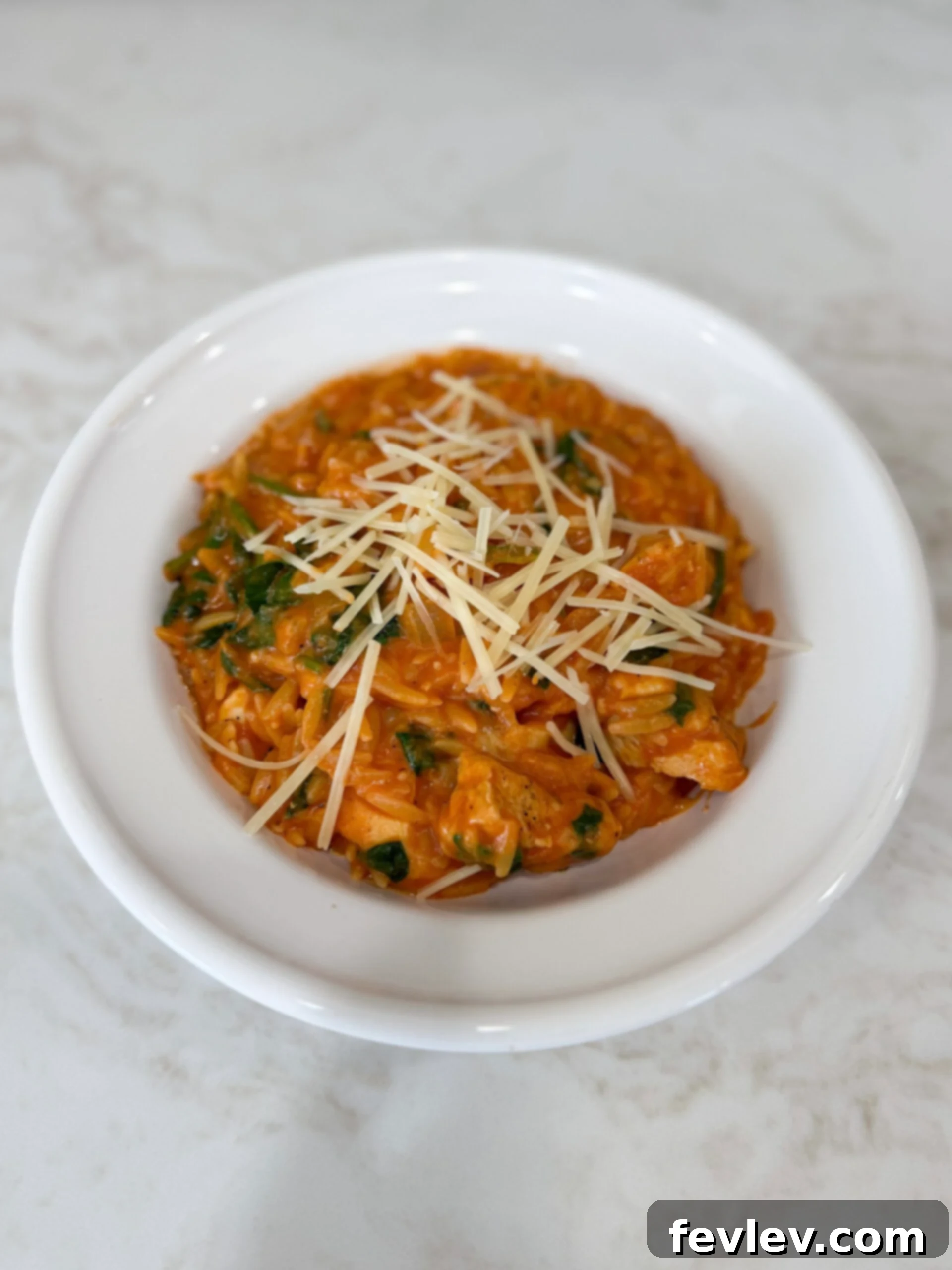 Creamy tomato chicken and spinach with orzo in a white bowl, generously topped with Parmesan cheese.