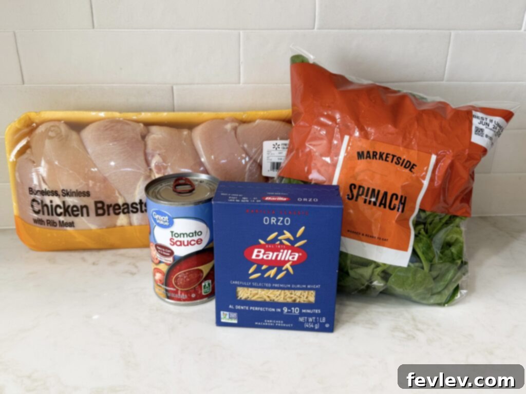 Ingredients laid out for making chicken and spinach with orzo: chicken, olive oil, butter, seasonings, orzo, tomato sauce, chicken broth, heavy cream, spinach, Parmesan.