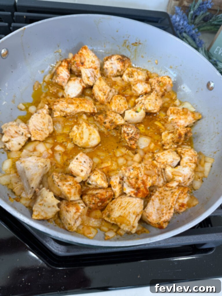 Cubed chicken breast, diced onion, and minced garlic sautéing in a large pot with oil and butter.