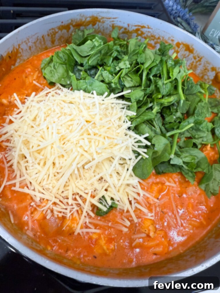 Fresh spinach and grated Parmesan cheese being added to the creamy tomato orzo with chicken.