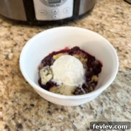 Low and Slow Berry Cobbler 2 A warm bowl of Slow Cooker Berry Cobbler topped with melting vanilla ice cream, ready to be enjoyed.