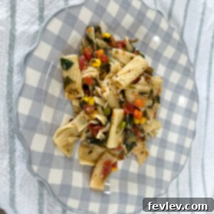 A vibrant and appetizing bowl of Veggie Pasta, featuring rigatoni tossed with colorful diced tomatoes, mixed vegetables, and fresh spinach, garnished with Italian cheese.