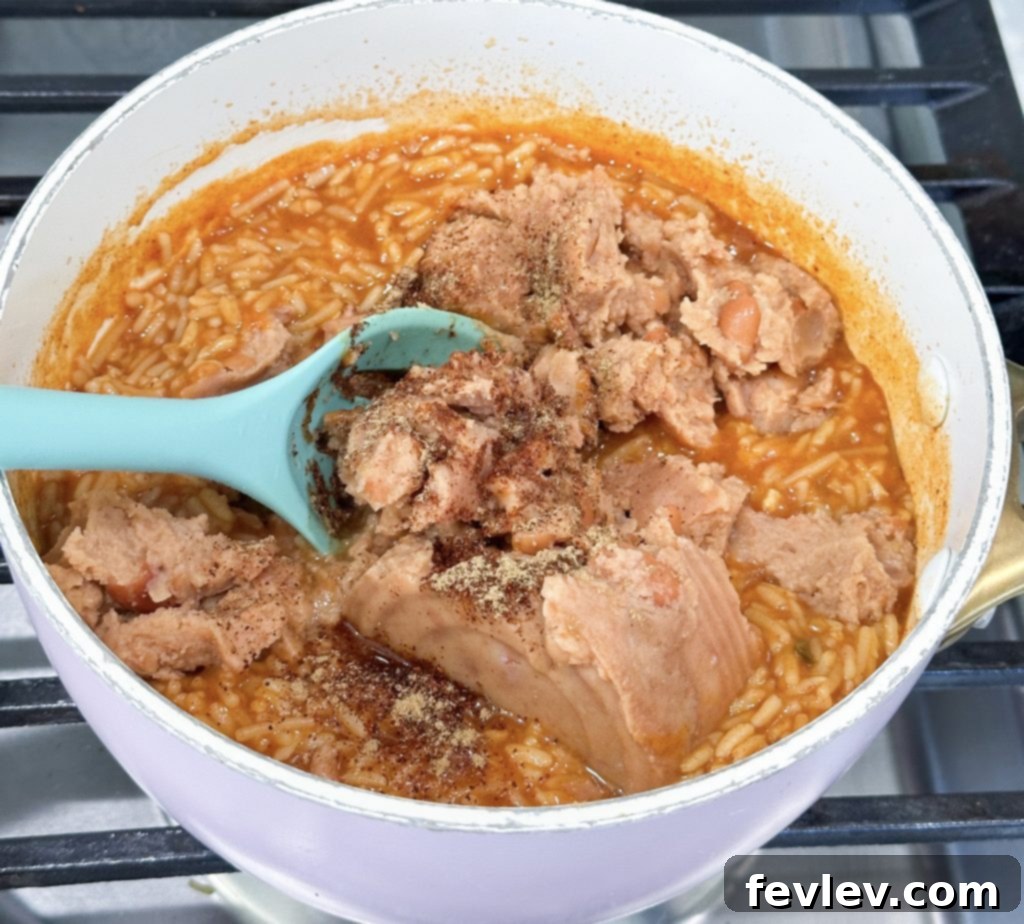 Mixing refried beans and spices into cooked rice for enchiladas