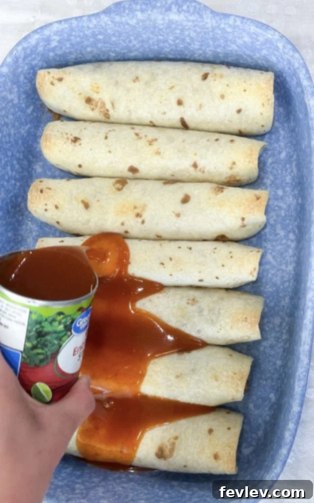 Pouring red enchilada sauce over baked bean and rice enchiladas