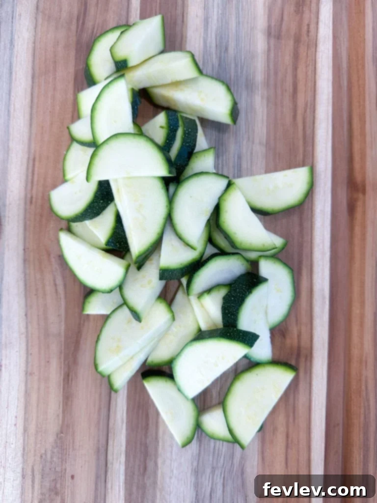 Bacon Tomato Pasta on a Budget 4 Fresh zucchini being sliced into half-moon shapes on a cutting board.