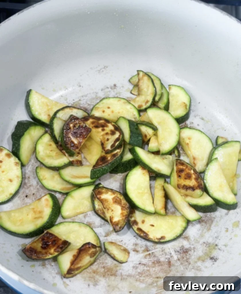 Bacon Tomato Pasta on a Budget 5 Zucchini pieces sizzling and browning in a hot skillet with olive oil.
