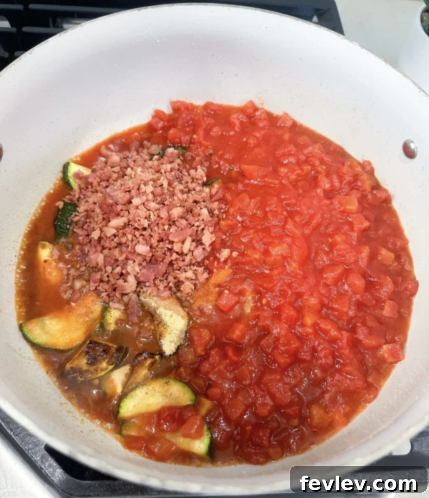 Bacon Tomato Pasta on a Budget 6 Tomato sauce simmering in a skillet with bacon bits and zucchini, covered to meld flavors.