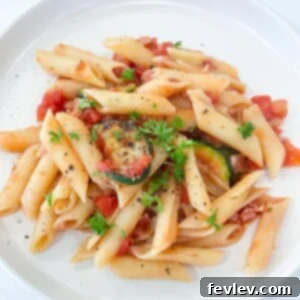 A delicious bowl of Tomato Bacon Pasta garnished with fresh basil leaves.