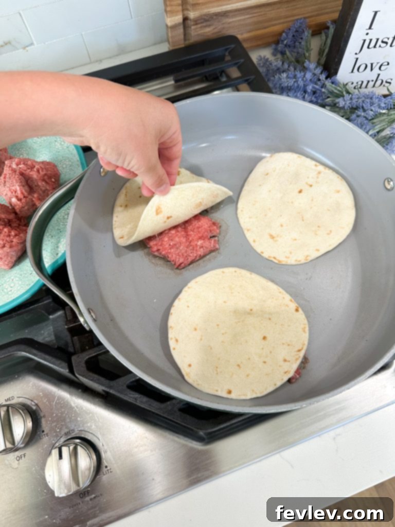 Ground beef being smashed with tortilla for hamburger tacos