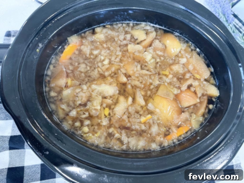 Cozy Slow Cooker Apple Cider 3 Cooked apples and oranges being mashed in a slow cooker, a key step for extracting maximum flavor for homemade apple cider.