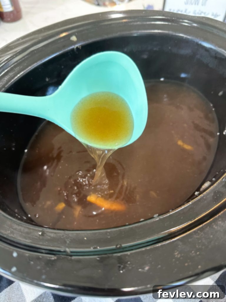 Cozy Slow Cooker Apple Cider 4 Freshly made slow cooker apple cider being poured from the crockpot into a clear glass pitcher, ready for serving.