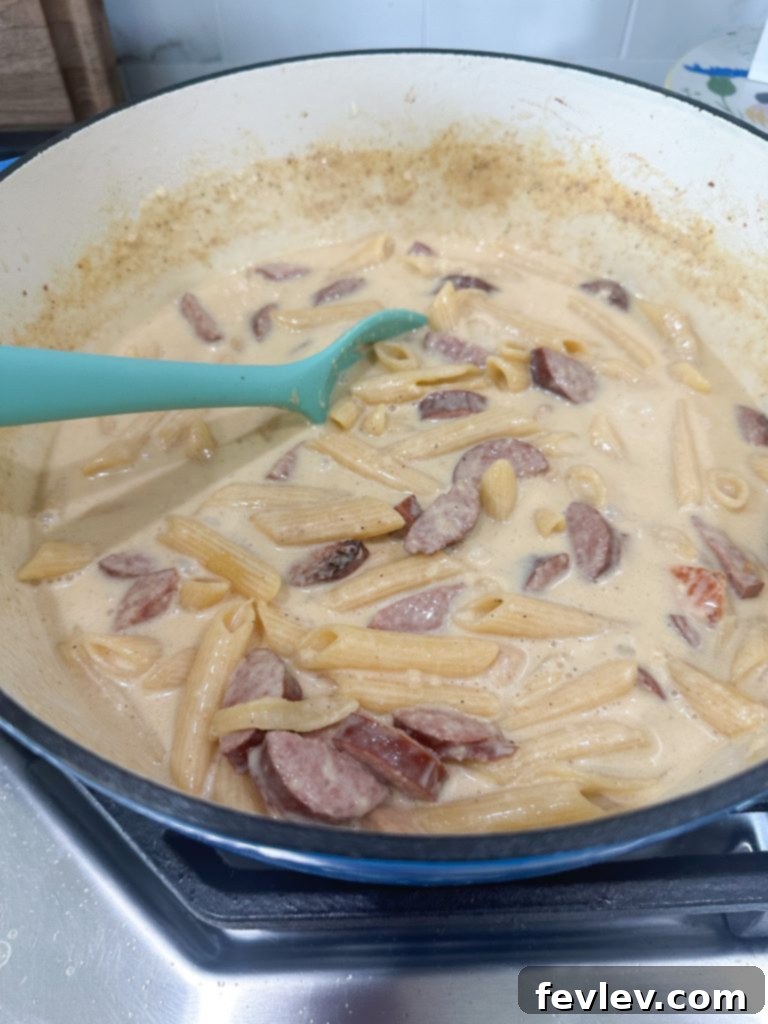 Adding minced garlic to cooked chicken and sausage mixture