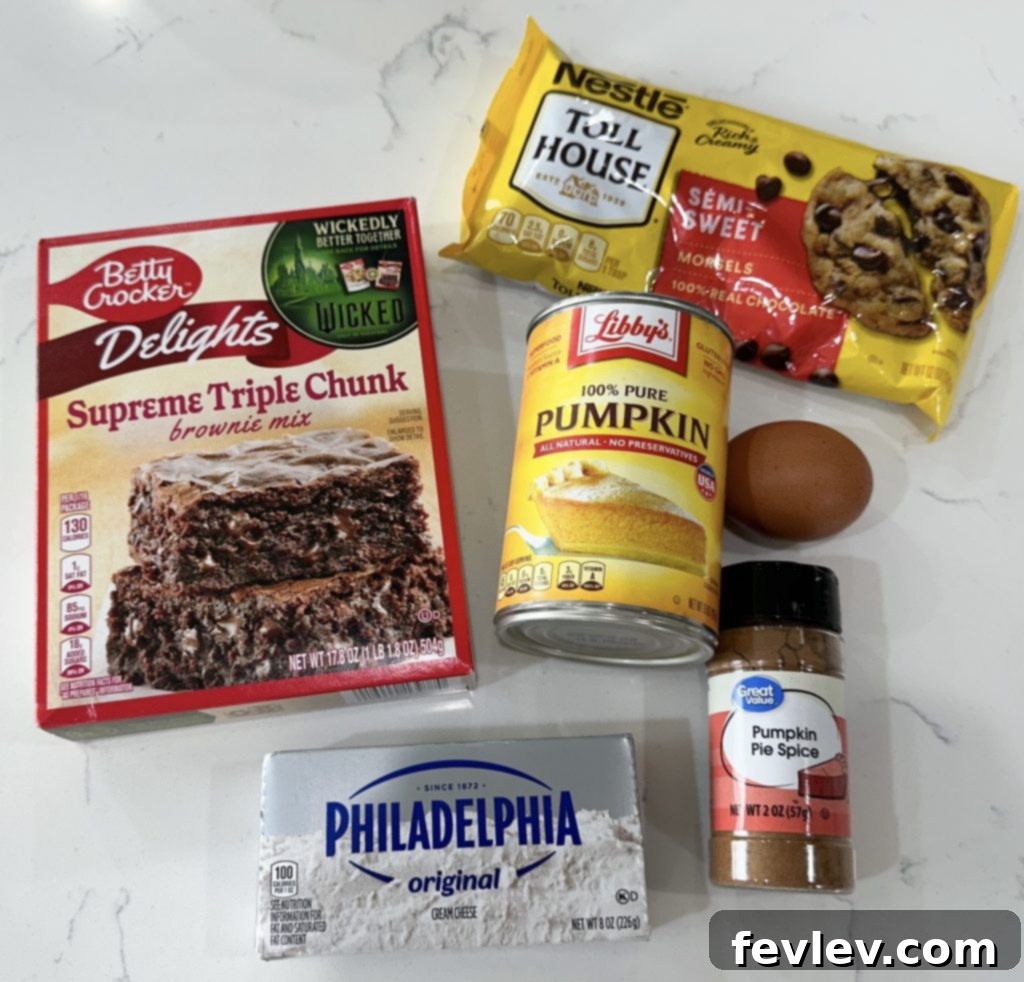 Ingredients for pumpkin brownies laid out on a table, including pumpkin puree, cream cheese, and brownie mix.