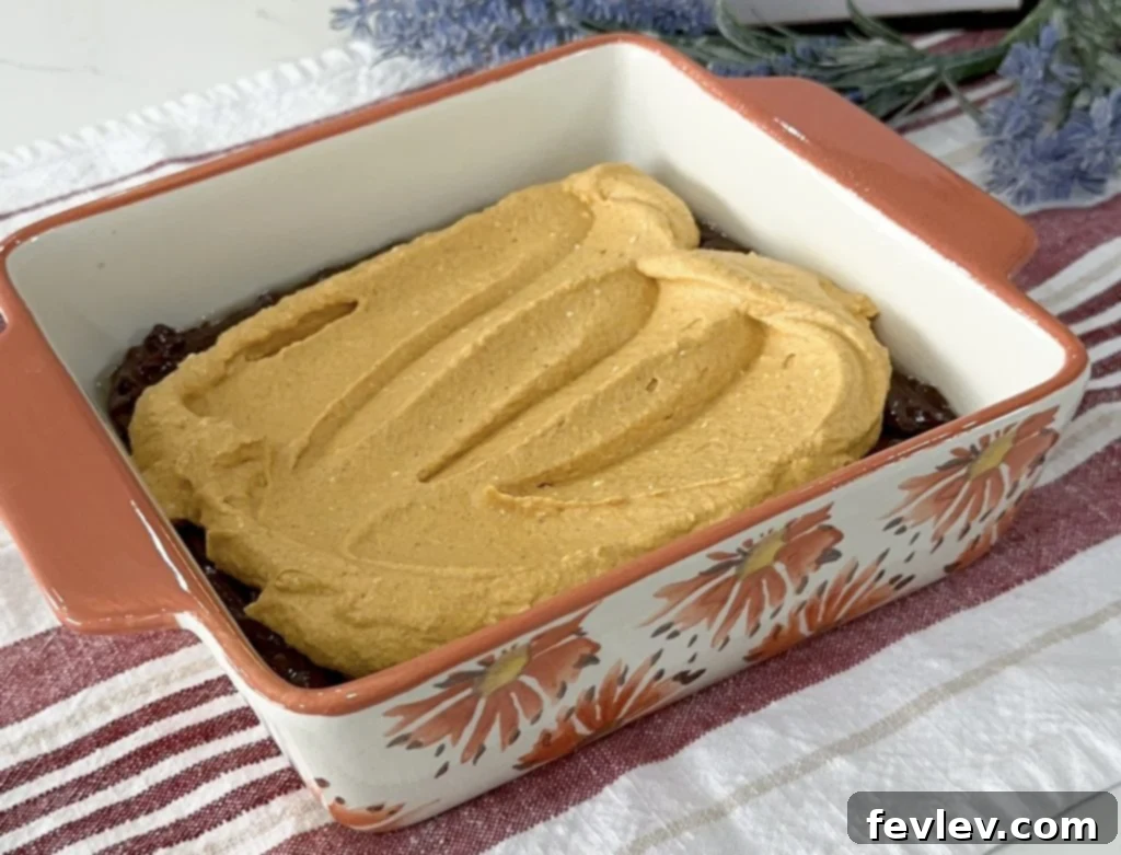 Pumpkin cheesecake mixture spread over the first brownie layer, showing distinct layers.