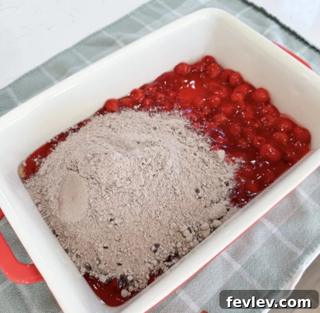 Layering dry chocolate cake mix over the sweet cherries in the baking dish for Black Forest Dump Cake
