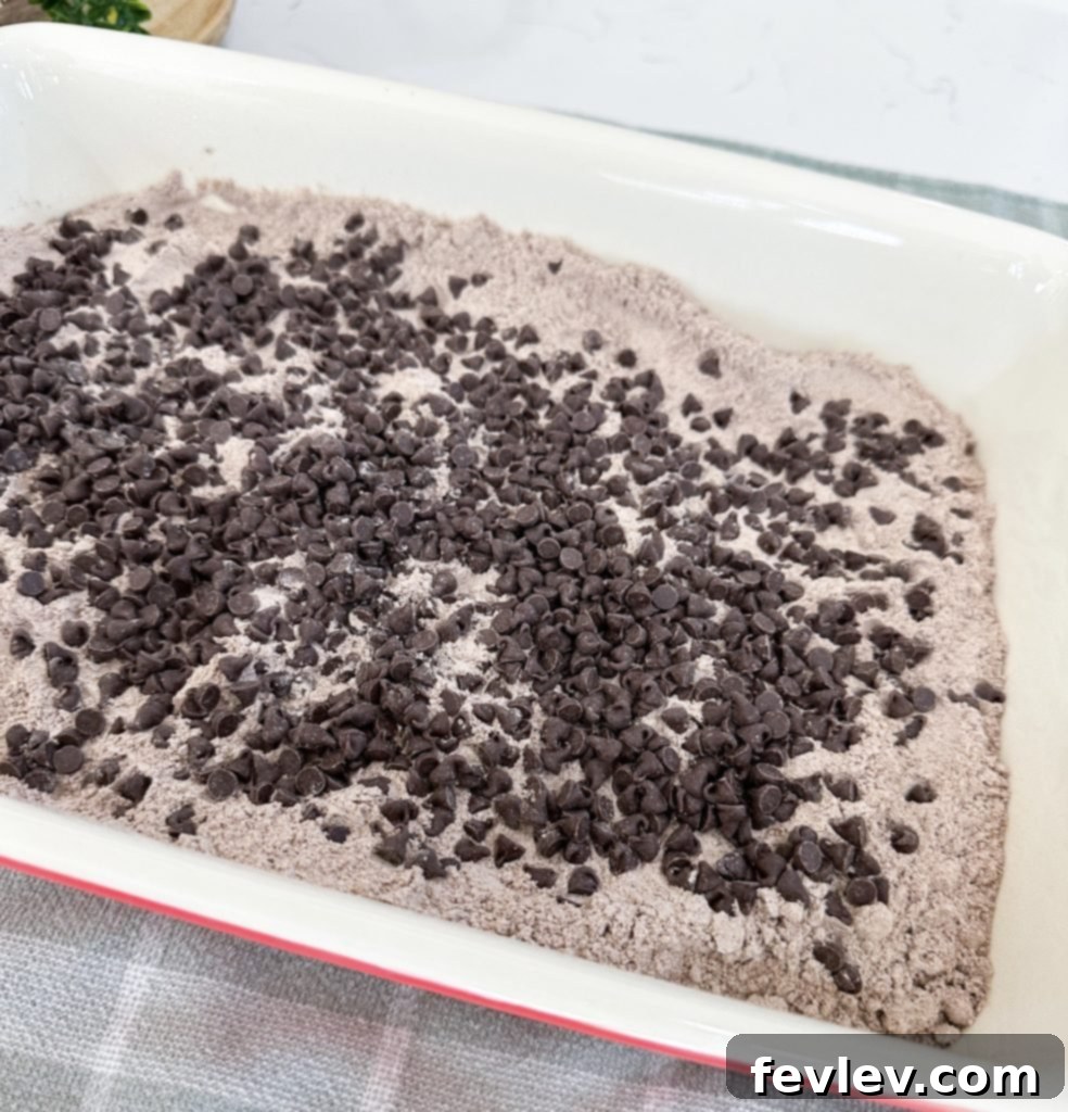Sprinkling chocolate chips generously over the dry cake mix layer of the Black Forest Dump Cake