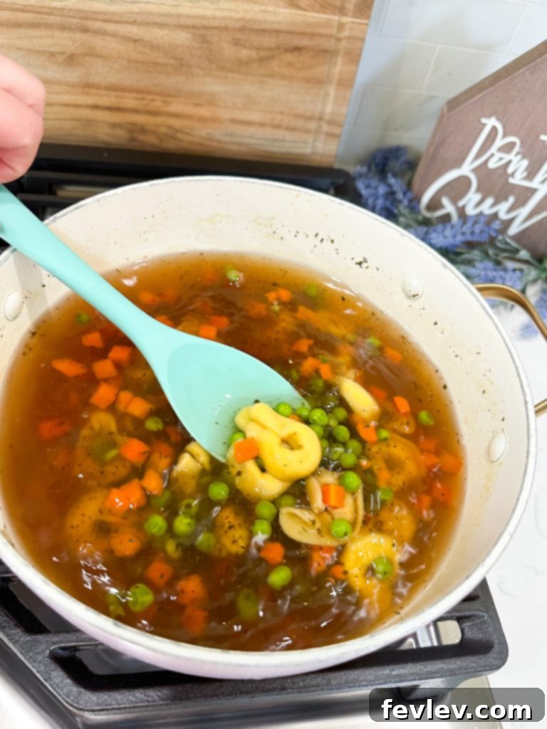 A large pot on a stovetop, filled with vegetable broth coming to a boil for the tortellini soup.