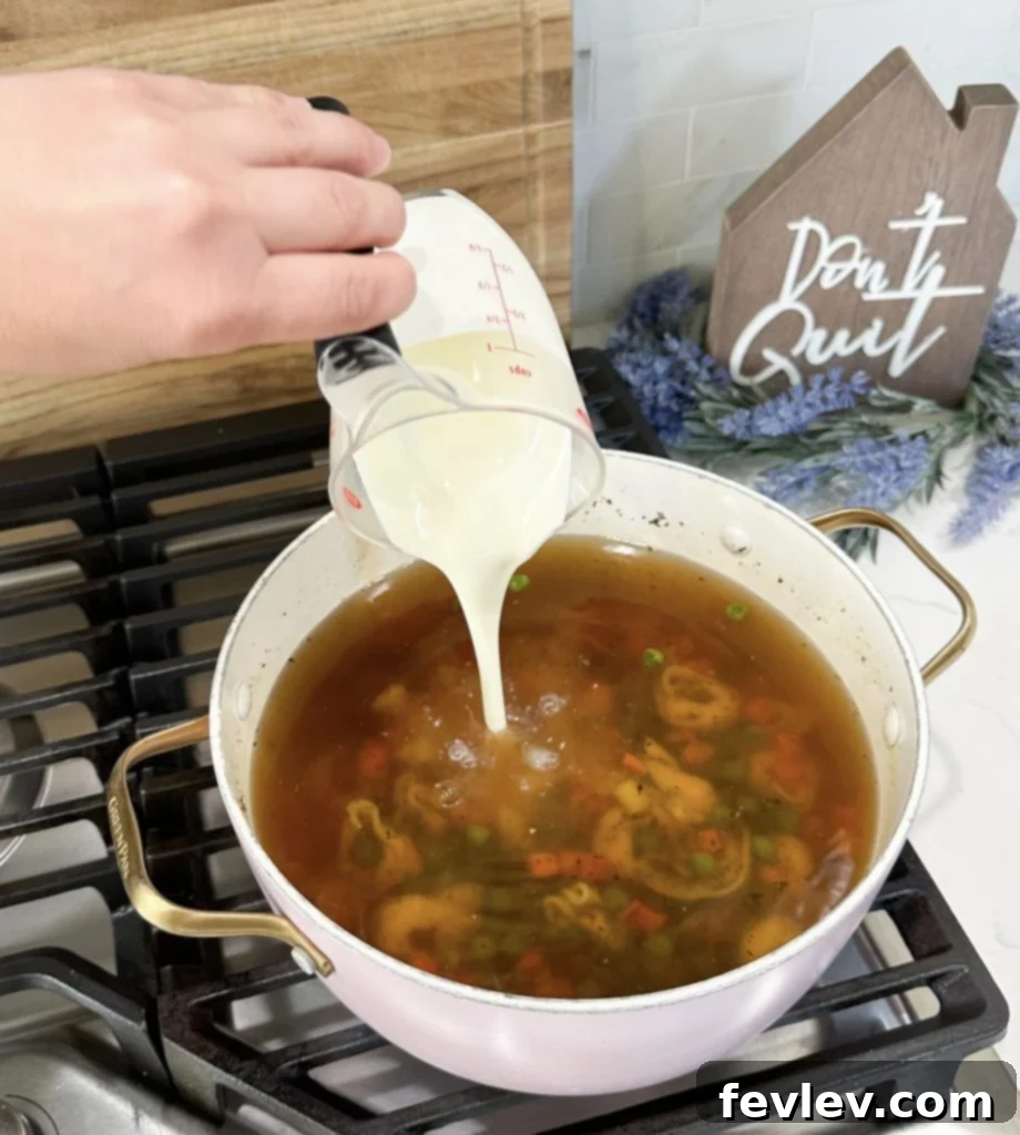 A close-up of the finished creamy tortellini soup in a large pot, showing tortellini, peas, and carrots in a rich broth.