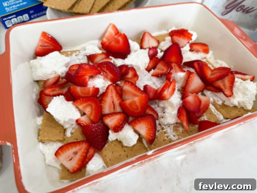 Layer of graham crackers covered with whipped topping in a layered strawberry icebox cake