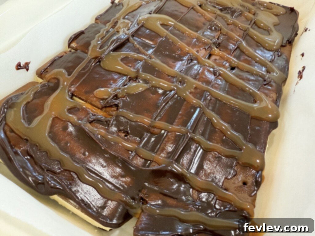 Hot fudge sauce being spread over the first layer of ice cream sandwiches in a baking dish, creating a delicious layered ice cream cake.