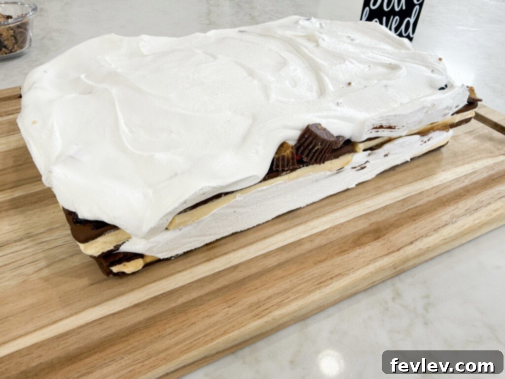 The second layer of whipped topping being smoothed over the fudge and ice cream sandwiches, completing the simple ice cream sandwich recipe layers.