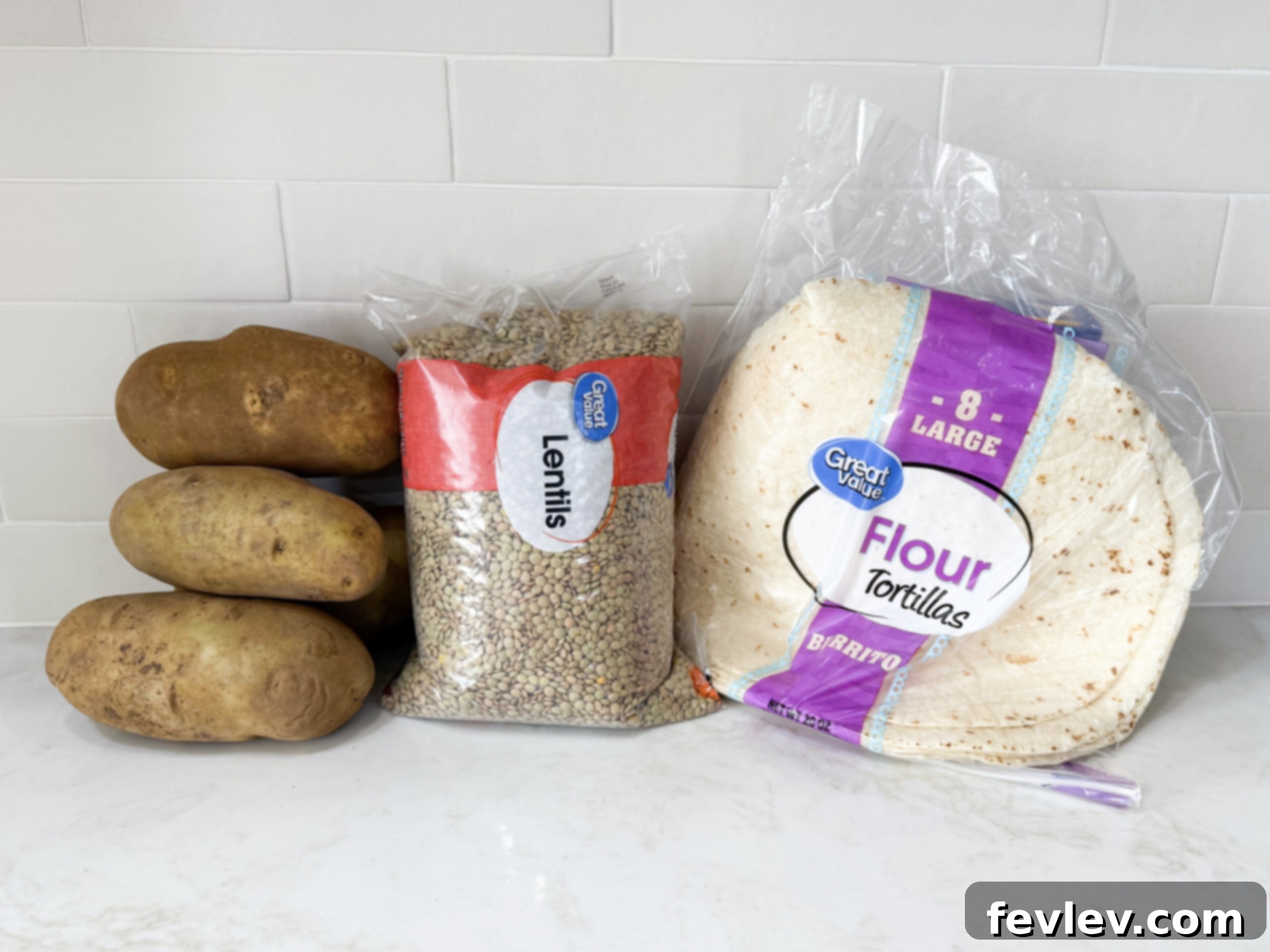 A selection of fresh ingredients laid out on a countertop, including lentils, potatoes, onions, and spices, ready for making burritos.