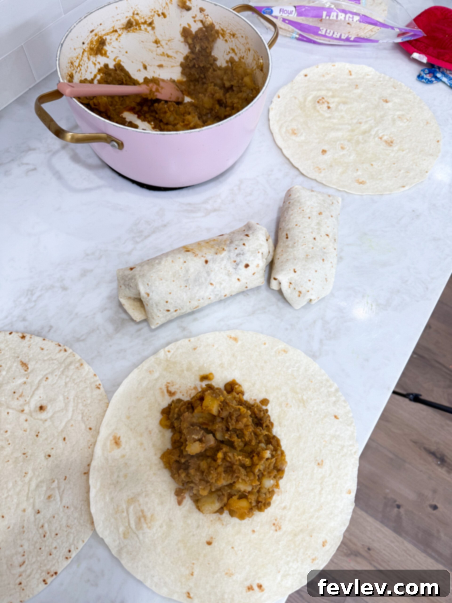 Scooping the lentil and potato filling into the center of a warm tortilla, preparing to roll a burrito.