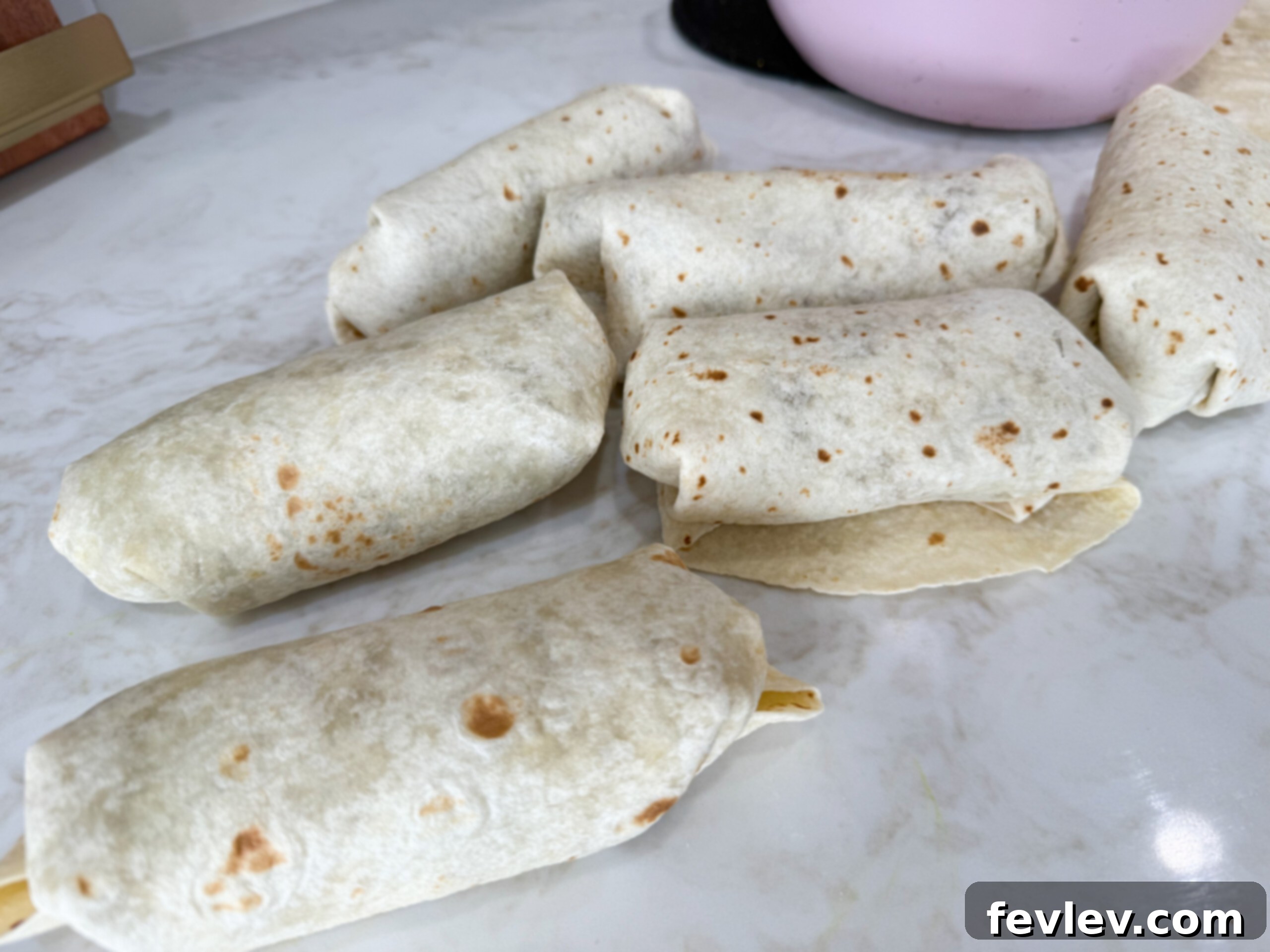 Several neatly rolled lentil burritos arranged on a countertop, ready for serving or storage.