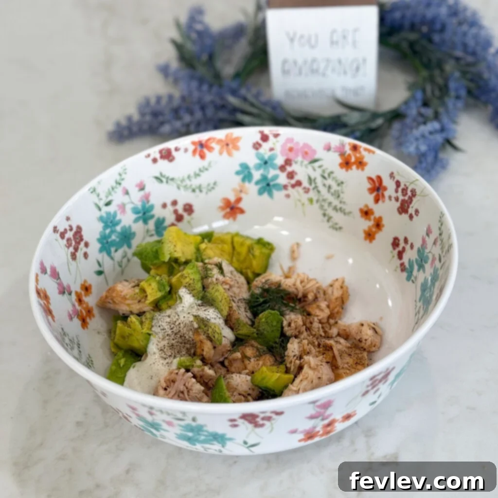 Combining diced chicken, avocado, ranch, and dill in a mixing bowl for chicken salad