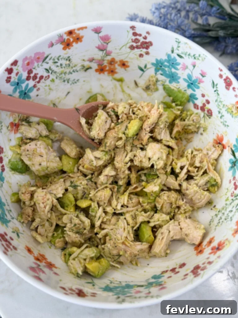 Mixing chicken salad ingredients until combined for a creamy texture