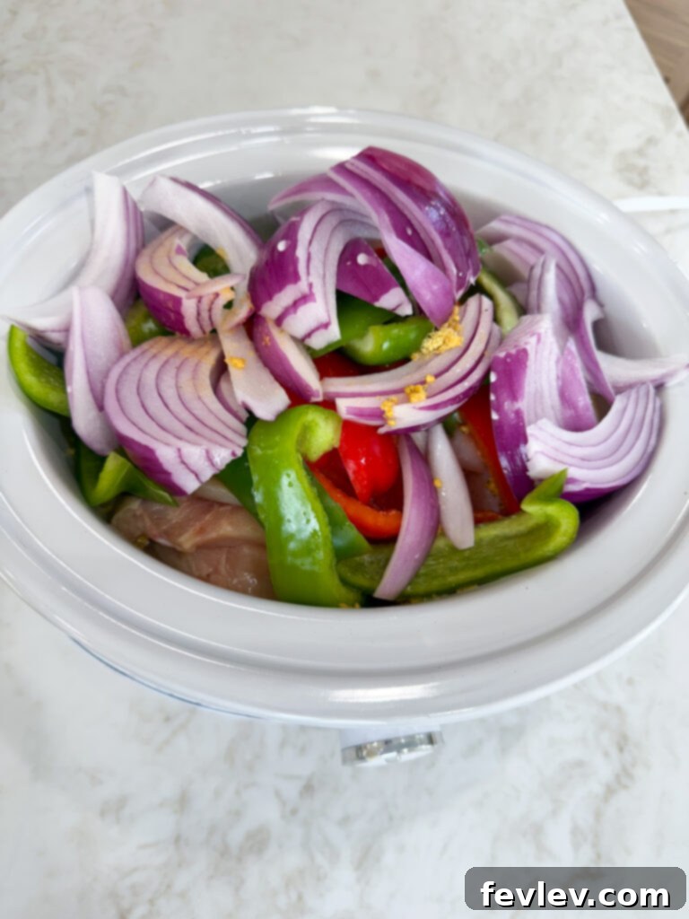 Adding ingredients to slow cooker for Crockpot Chicken Philly Cheesesteak Sandwiches