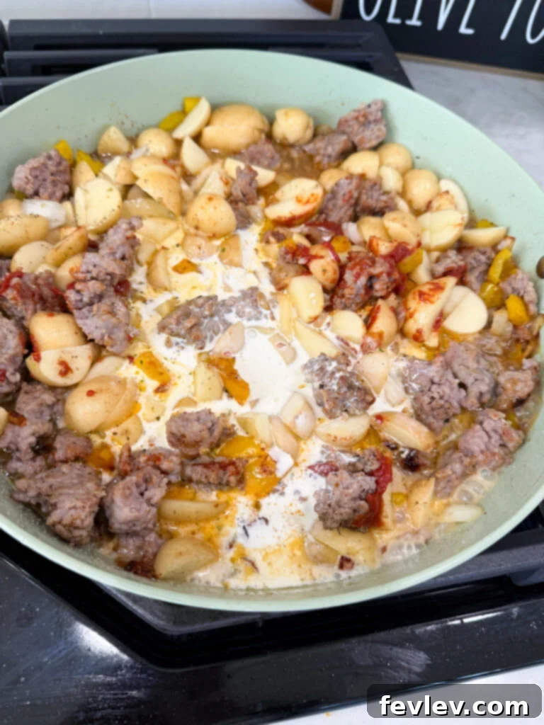 Pouring heavy cream into the skillet with sausage and potatoes