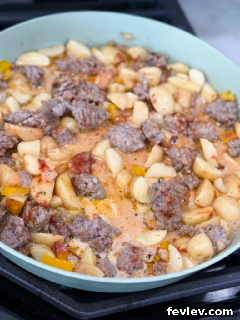 Creamy sauce simmering with Italian sausage and potatoes in skillet