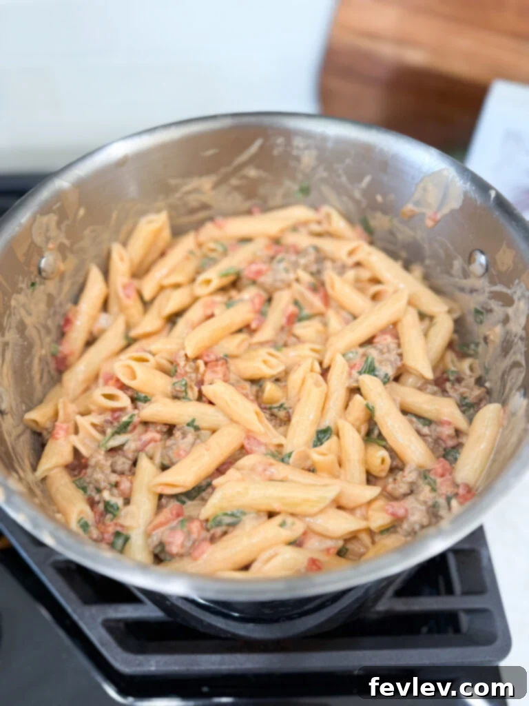 Mixing cooked pasta with creamy Italian sausage sauce