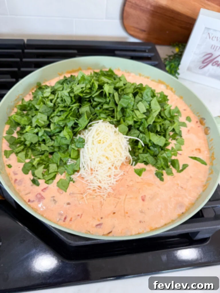 Fresh spinach wilting into the creamy sausage pasta sauce
