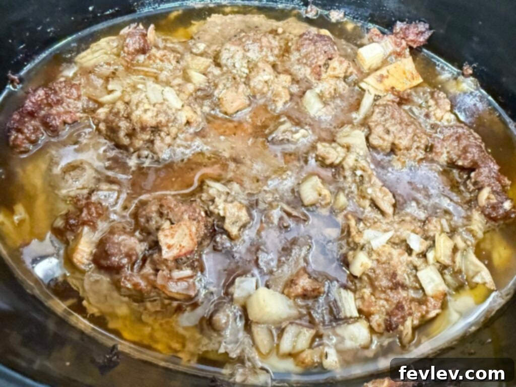 Cooked ground meat browned in a black slow cooker, ready to be drained.