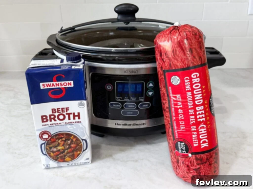 Large slow cooker on a white counter with beef broth and package of ground beef, ready for cooking.