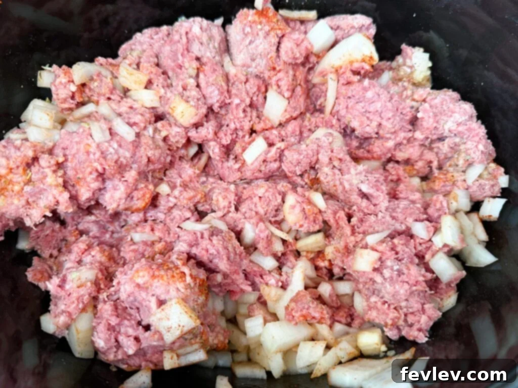 Ground beef and onion mixture placed evenly in a black slow cooker.